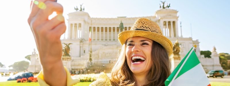 Happy young woman with italian flag making selfie on piazza venezia in rome, italy