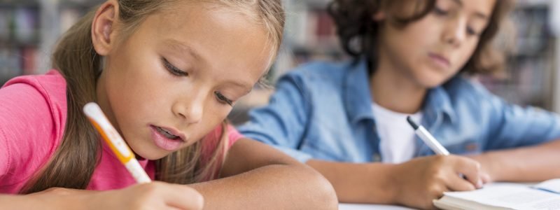 Duas crianças estudando juntas e escrevendo em seus cadernos, ilustrando a adaptação escolar na Itália.